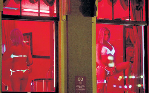 В каждом из окон квартала красных фонарей стоит девушка и манит прохожих в свою крошечную комнатку